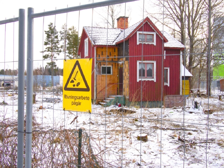 Rött hus, stängsel och en gul skylt där det står rivning pågår.