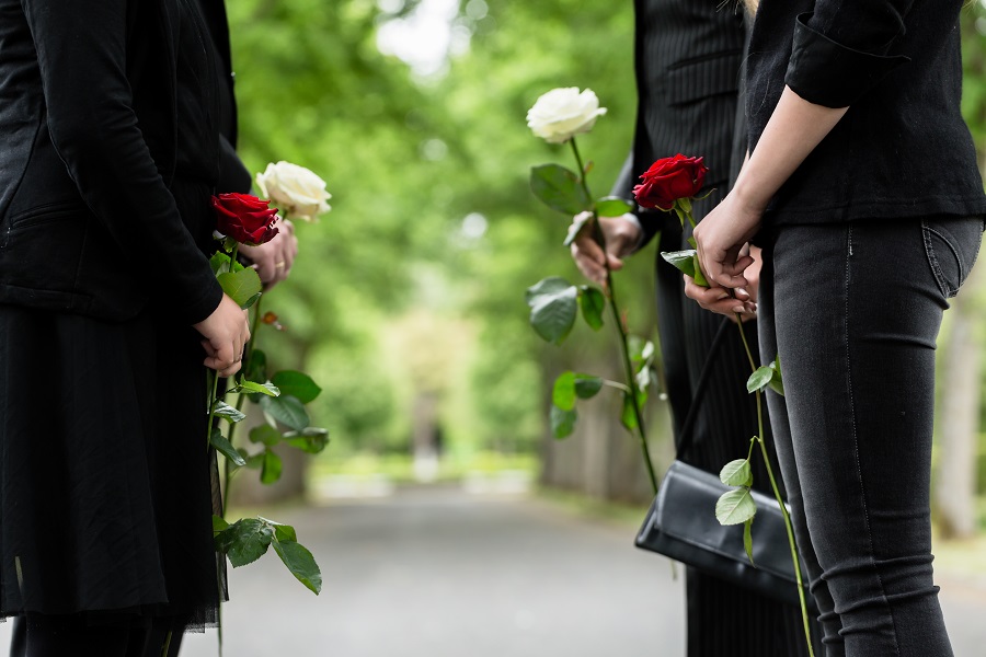 Svartklädda personer på begravning med rosor i sina händer.
