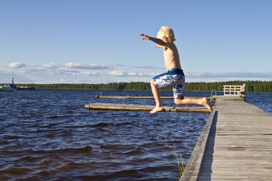 Pojke hoppar i vattnet från brygga.