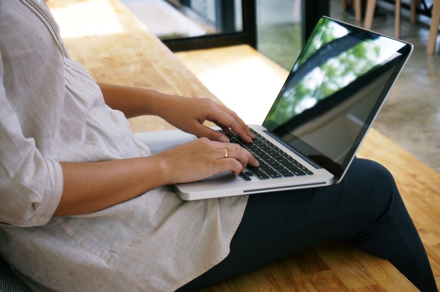 Kvinna sitter i soffa med bärbar dator i knät