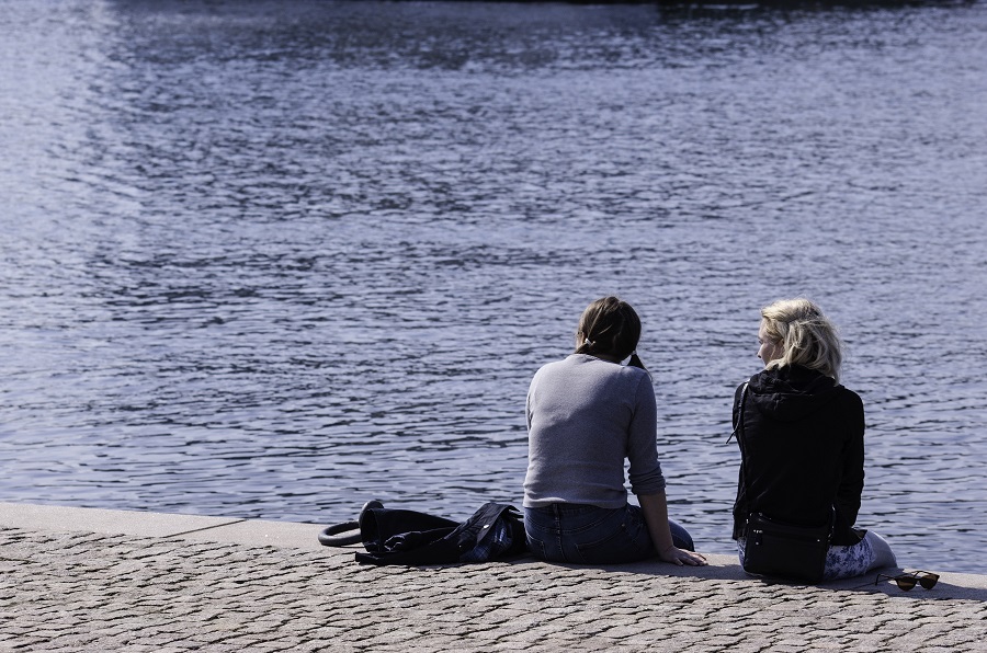 Två unga kvinnor sitter bredvid varandra vid vattnet.