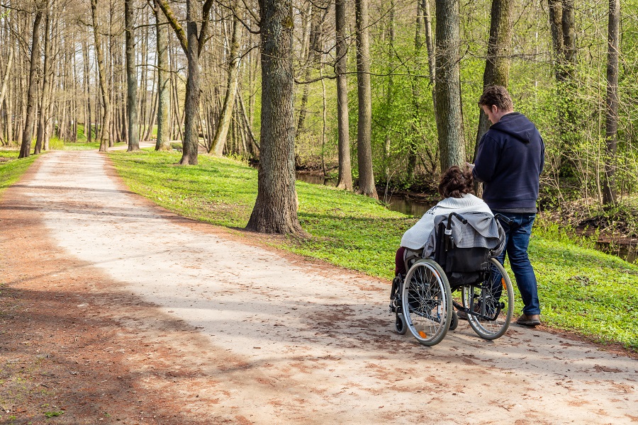 Kvinna i rullstol på en stig i skogen tillsammans med personlig assistent.