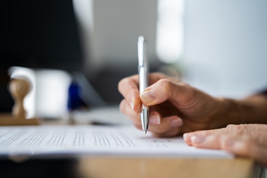 Närbild av hand som håller i penna och skriver under ett dokument.